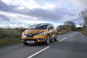 metallic orange renault scenic estate driving on tarmac road with green trees and grass on either side