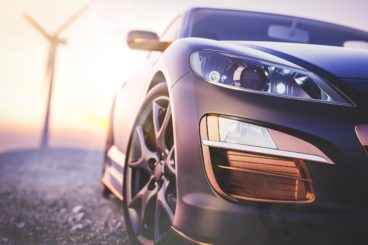 The image in front of the sports car scene behind as the sun going down with wind turbines in the back.