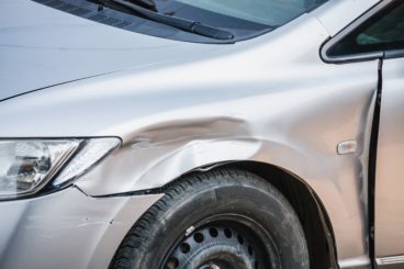 silver car that has been in a crash and now has a dent just above the wheel