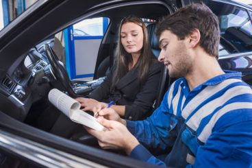 Car expert shows the checklist of repaired items to customer in garage
