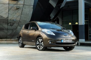 metalllic nissan leaf parked on tarmac with mirrors and modern building in the background