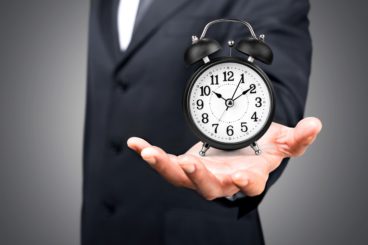 Man holds alarm clock out in front of him.