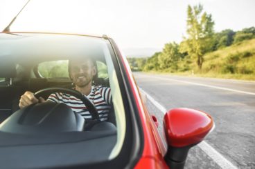 Happy smiling driver man in new red car on the road.