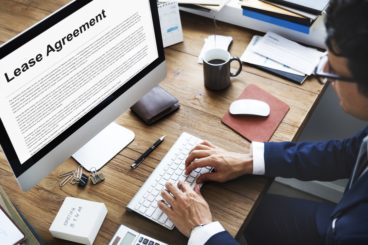 Man wearing glasses typing on his computer and currently working on a lease agreement