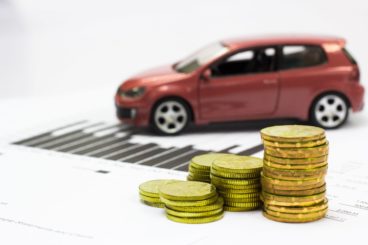 Red car with piles on gold money in foreground. Van leasing for self-employed