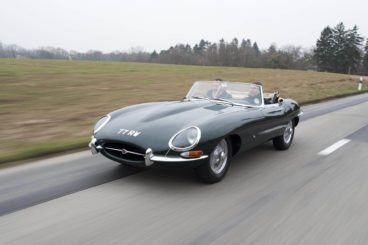 Jaguar E-Type in dark green travelling fast on a road