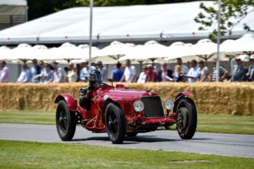 Red Maserati Tipo M on a race track with a crowd in the background
