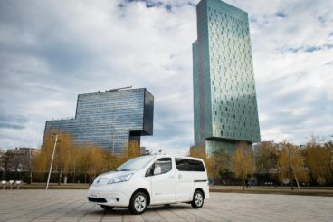 White Nissan e-NV200 electric van parking on paved road with big city in the background
