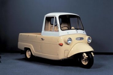 Old yellow three wheeled Mitsubishi vehicle on a blue background