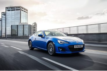 Blue Subaru BRZ driving on a road with modern buildings in the background