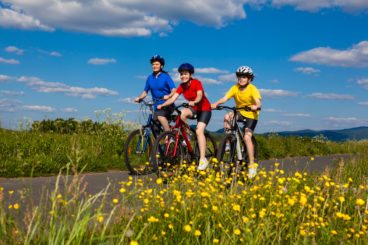 family in brightly coloured clothing cycling along a country road on a sunny day
