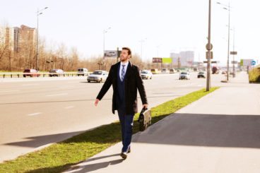 man in a suit with a briefcase walking along the pavement on a sunny day