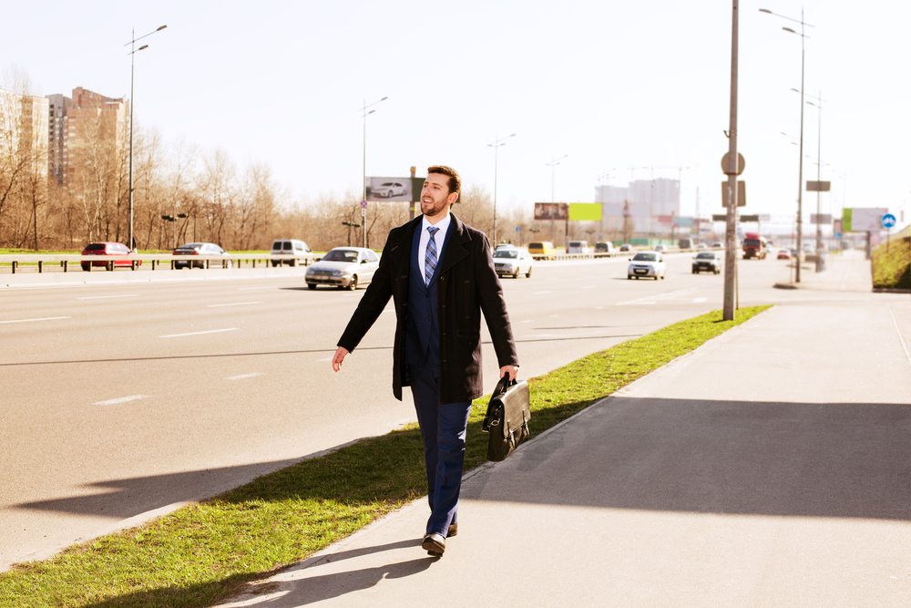 man in a suit with a briefcase walking along the pavement on a sunny day