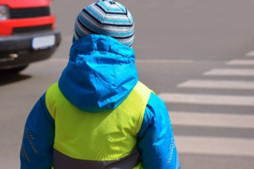 Little boy wearing a reflective safety vest whilst crossing the road.