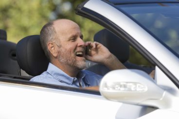 A senior man driving a car whilst on a cell phone