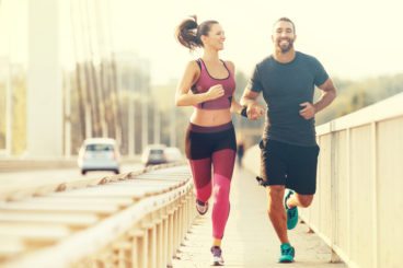 two runners running along a bridge behind barriers smiling