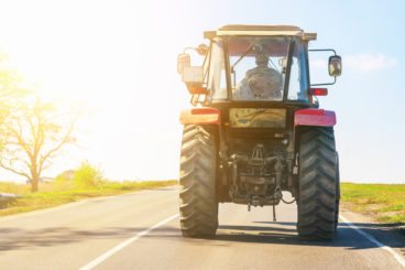 red tractor driving along a country road in the sunshine