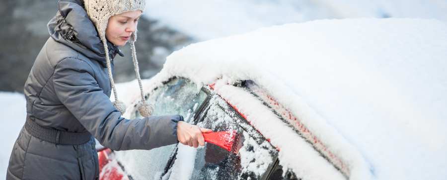 Woman using a scraper to remove ice from car windows