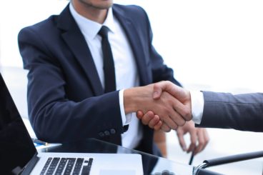 handshake business partners in front of the open laptop
