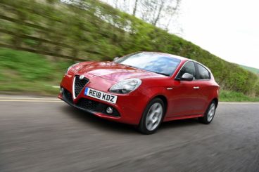 a red Alfa Romeo Giulietta Diesel Hatchback driving on tarmac with blurred trees in the background