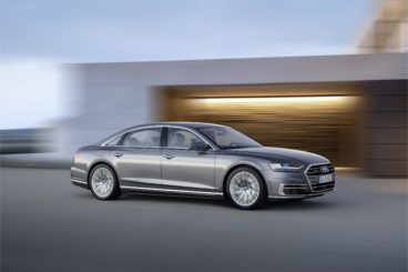 a metallic grey audi a8 diesel saloon driving on tarmac road with blurred background