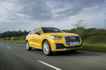 a yellow audi q2 estate driving on tarmac road with blurred trees in the background