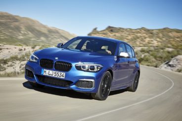 a metallic blue bmw 1 series diesel hatchback driving on tarmac road in dessert setting