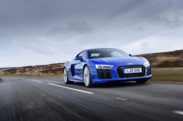 a bright blue audi r8 coupe driving on tarmac road with grass field in the background