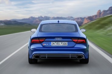 a metallic blue audi rs7 sportback driving away on tarmac road with big mountains in the background