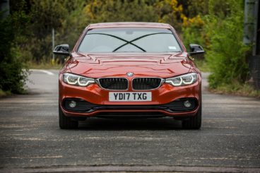 a metallic bmw 4 series diesel coupe driving on tarmac road with green trees on either day