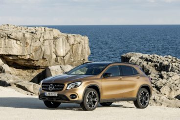 a metallic coloured mercedes GLA Class paked on sand with rocky beach behind it