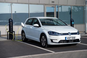 a metallic white volkswagen e golf parked in space plugged into charging station
