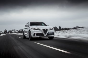 a metallic white Alfa Romeo Stelvio Diesel driving on tarmac with snow covered fields on either side