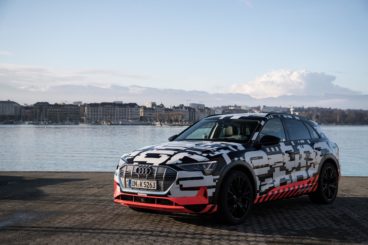 a black, white and red patterend BMW e-tron parked on pavement infront of lake