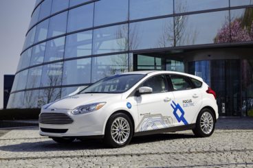 a white ford focus electric parked on pavement infront of modern building