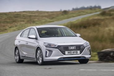 a silver hyundai ioniq electric driving on tarmac road with green hills in the background