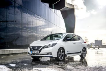 White Nissan Leaf in front of glass building