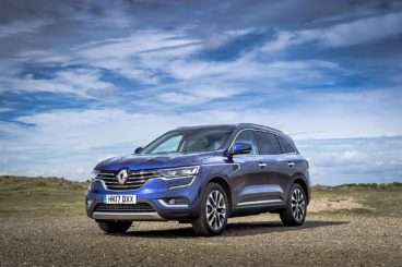 a metallic blue Renault Koleos parked on gravel on a sunny day