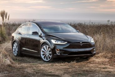 a dark coloured tesla model x parked in field