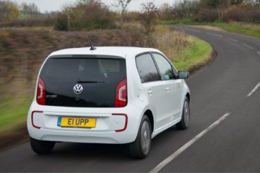 a white volkswagen e-Up! with red detailing driving on tarmac country road