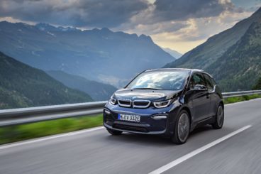 a dark coloured BMW i3 Rex driving on tarmac road with mountains in the background
