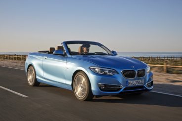 a metallic blue bmw 2 series diesel convertible with the roof down driving on tarmac road