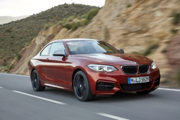 a metallic bmw 2 series diesel coupe driving on tarmac road with rocky mountains blurred in the background