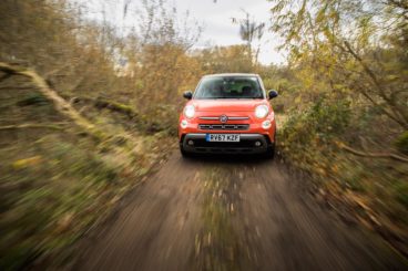 a metallic orange fiat 500l diesel hatchback driving quickly through forest setting