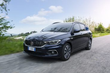 a dark coloured fiat tipo hatchback driving on tarmac road with greenery in the background