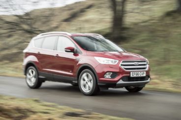 a maroon ford kuga diesel estate driving on tarmac road with blurred trees in the background