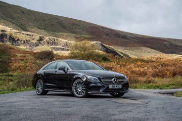 a black mercedes CLS parked on tarmac will tall grassy hills in the background