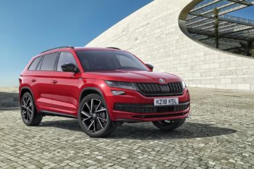 a solid red Skoda Kodiaq parked on paving with modern building in the background