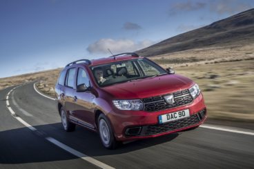 a dark red dacia logan MCV Stepway estate driving on tarmac road with grassy hills in the background