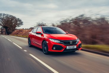 a bright red honda civic diesel hatchback driving on tarmac road with blurred trees in the background